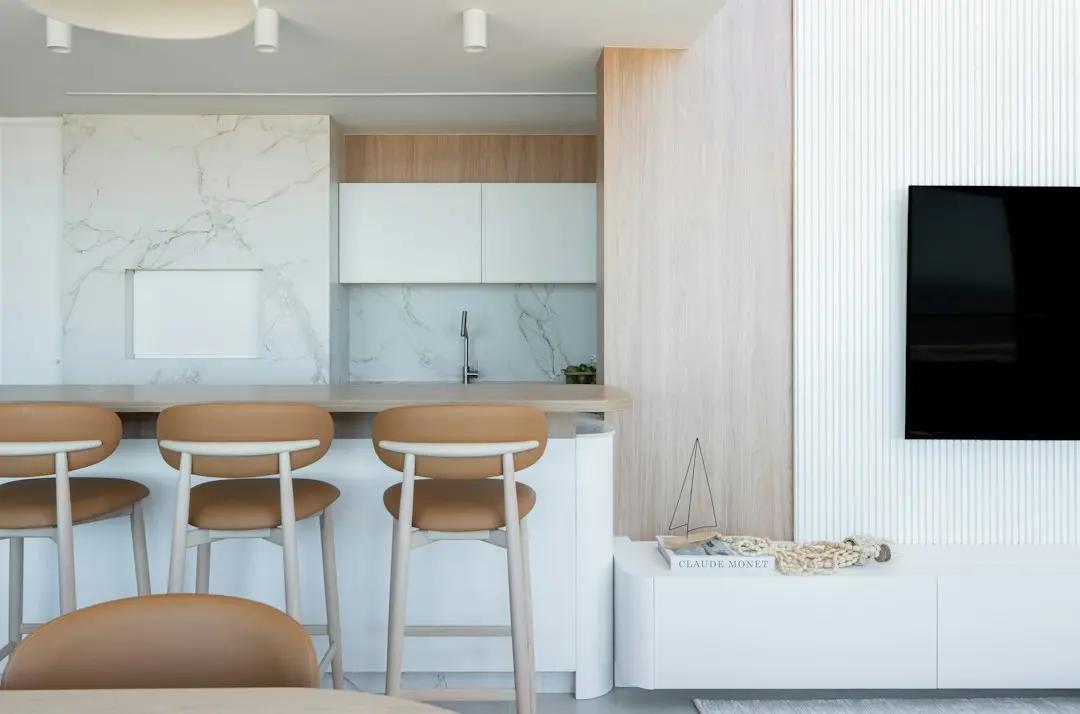 A wall-mounted flat-screen TV next to a kitchen bar in a bright living room: the kind of screen the Drogon TV app runs on